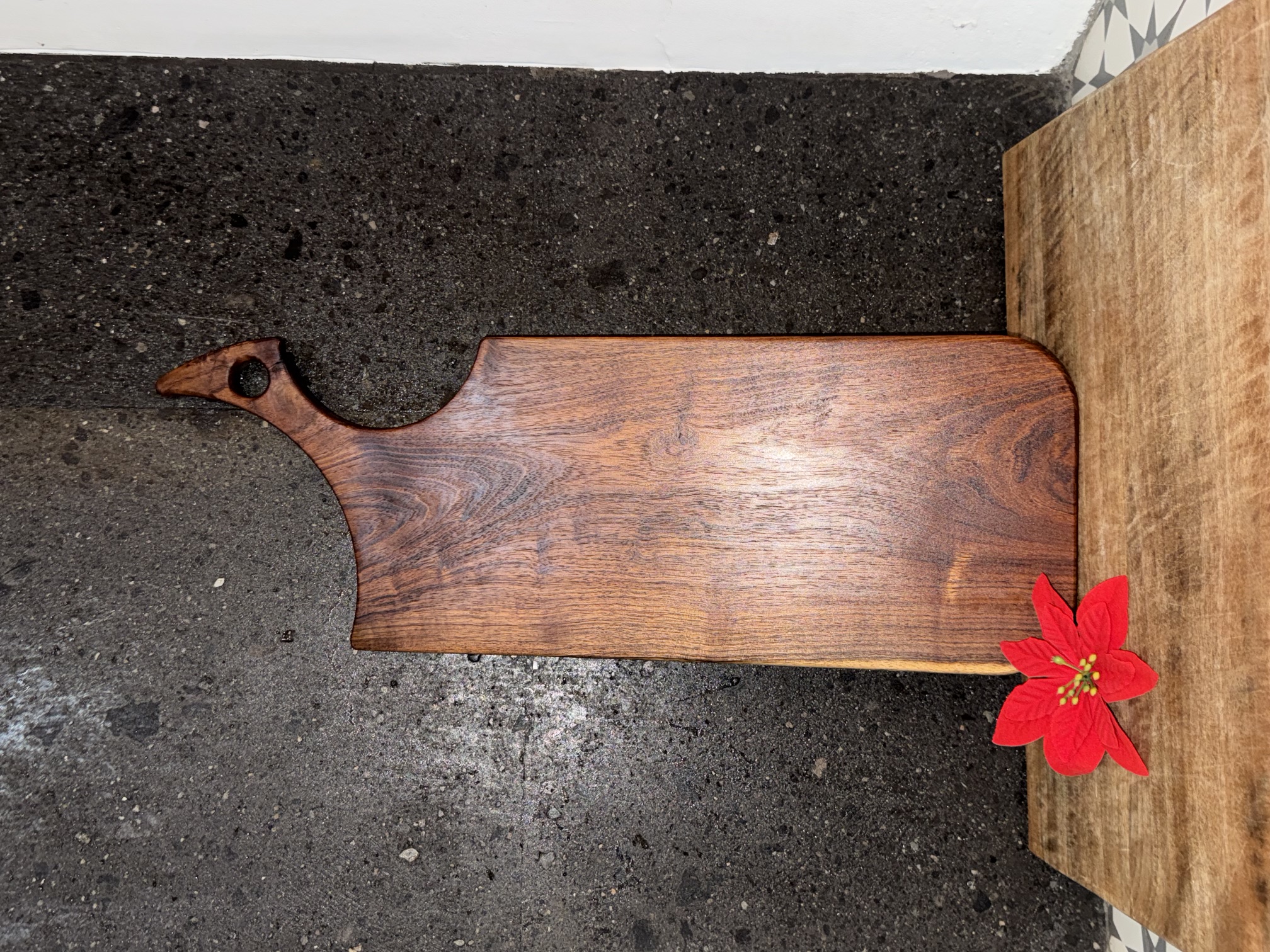 Tabla de silueta orgánica con un mango curvo, veta continua de madera clara a oscura.
