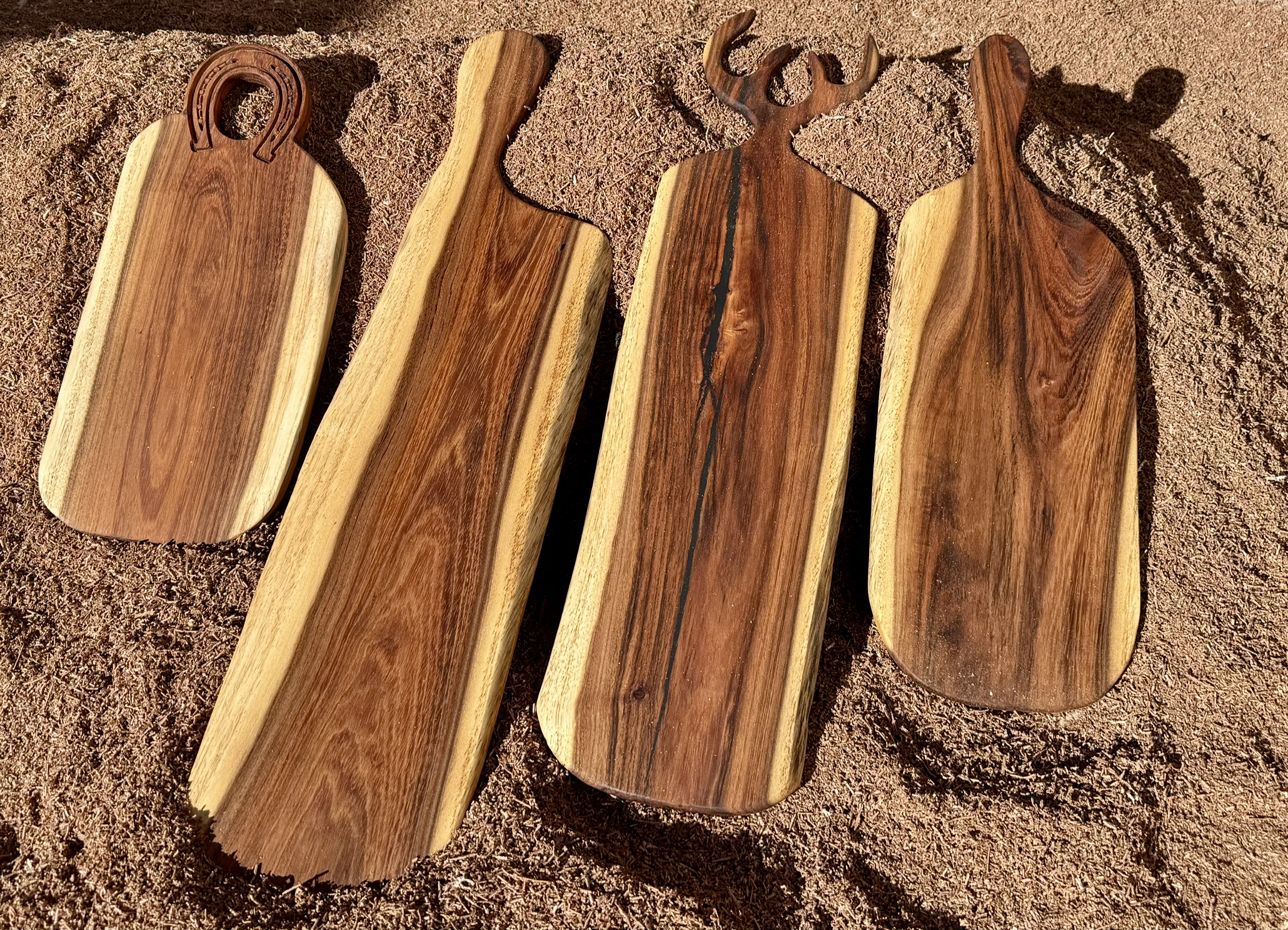 Cuatro tablas de madera maciza recién talladas, con formas de herradura y mango, recargadas sobre un panel de madera rústica.