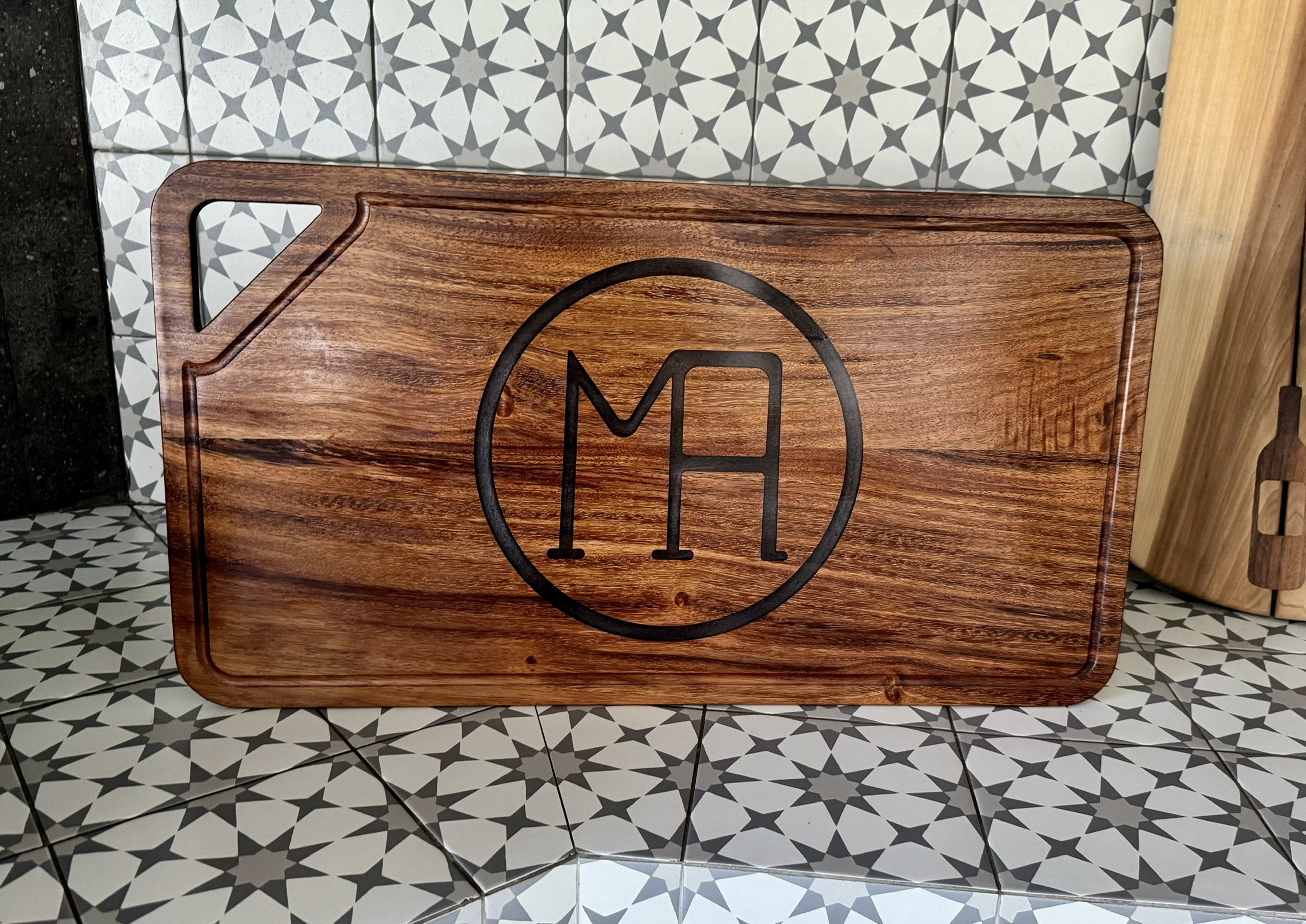 Tabla de cocina grabada con las iniciales M y A dentro de un círculo.