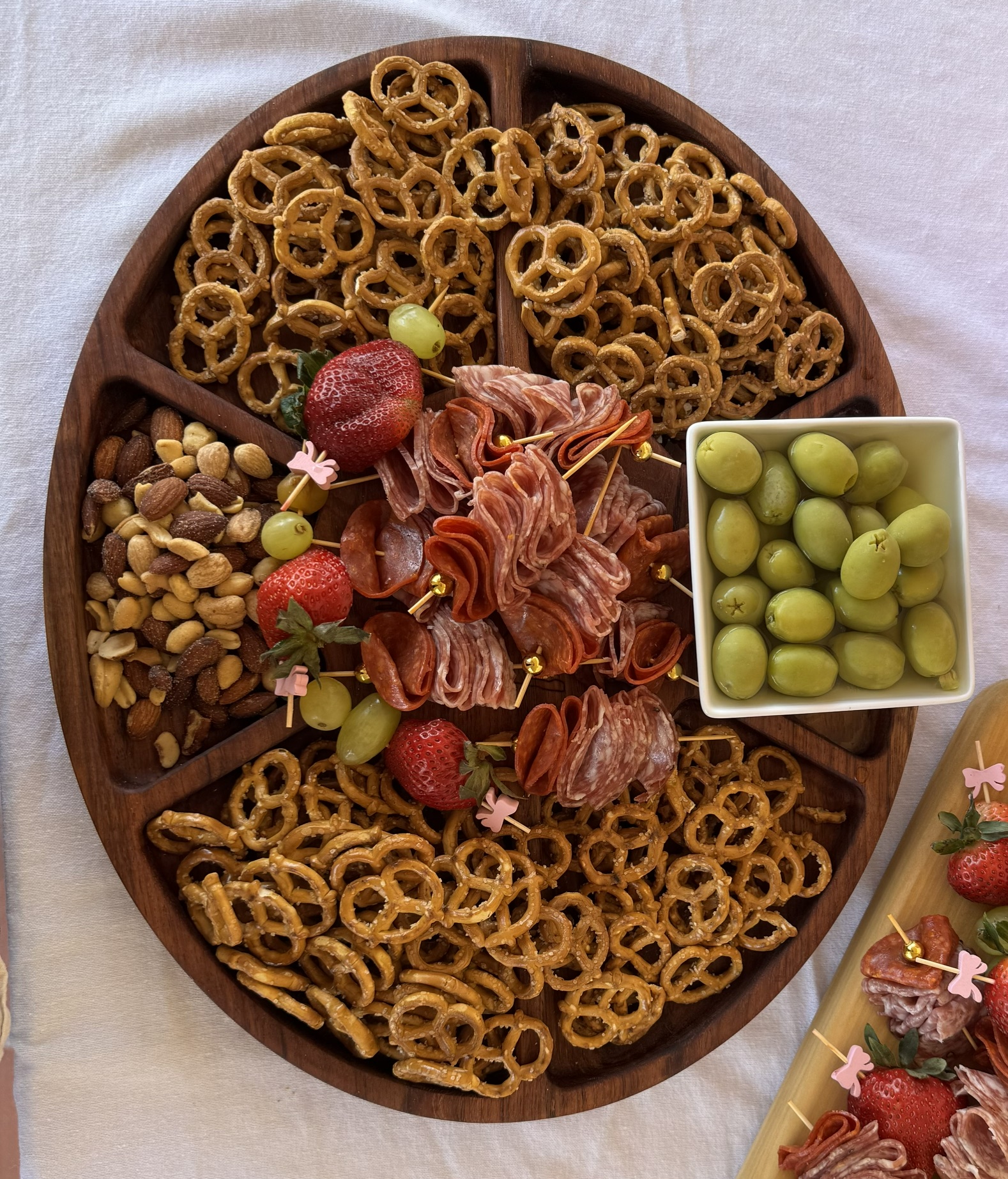 Tabla circular dividida en secciones, servida con pretzels, botanas y embutidos.