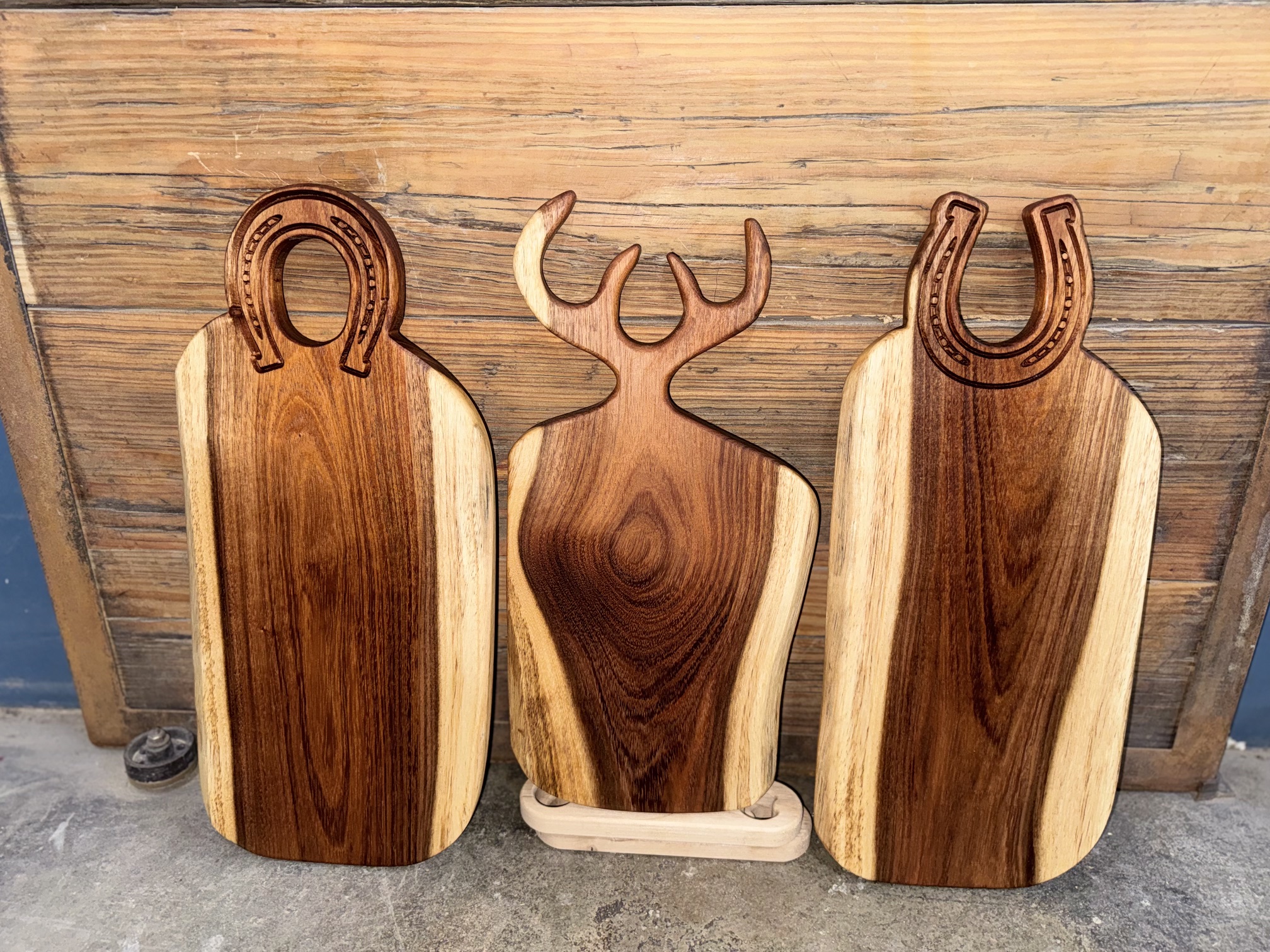 Tres tablas talladas con formas de herradura y cornamenta, recargadas sobre un muro de madera.
